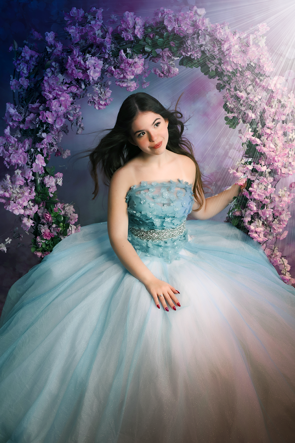 Book debutante com ensaio 15 anos em estúdio, mostrando debutante de vestido azul rodado em cenário com arco de flores para book 15 anos no Estúdio Roni Sanches.
