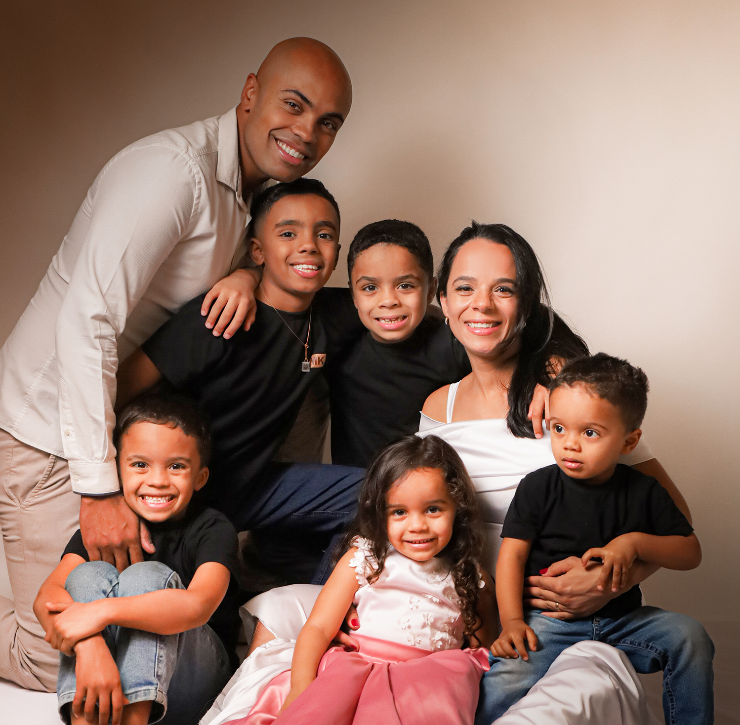 Ensaio gestante em família em SP: pais e cinco filhos abraçados e sorrindo em estúdio fotográfico.